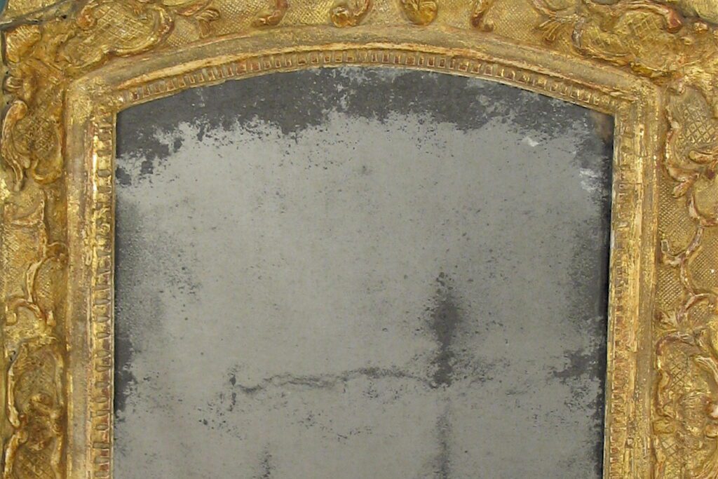 A mirror with gold leaf frame and a silver background.