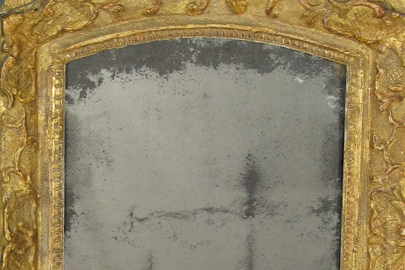 A mirror with gold leaf frame and a silver background.