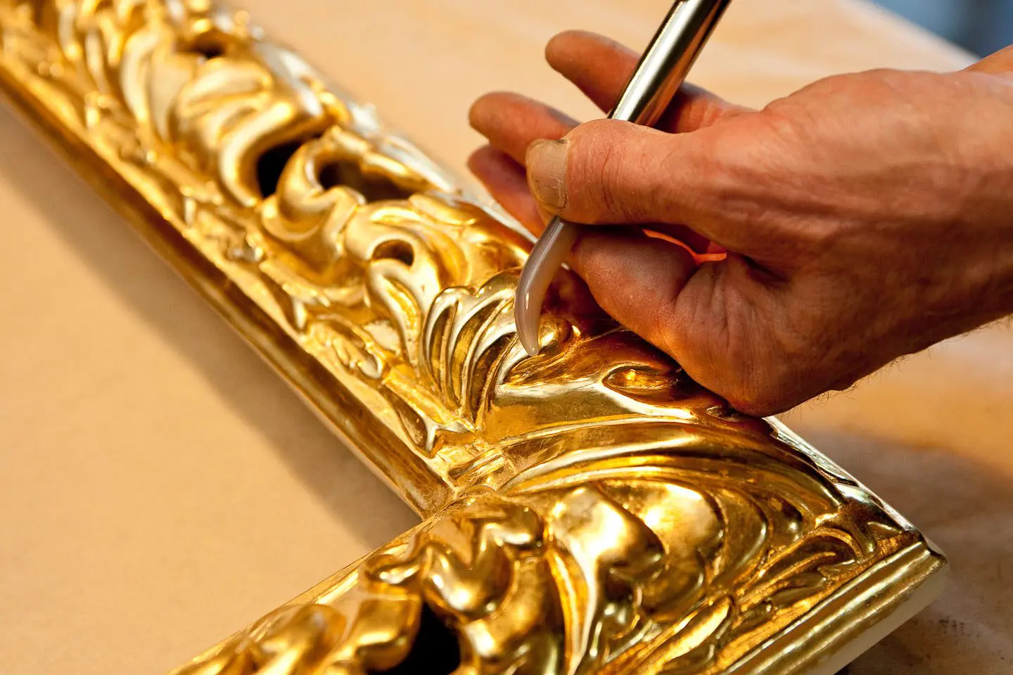 A person is painting the gold frame of a picture.