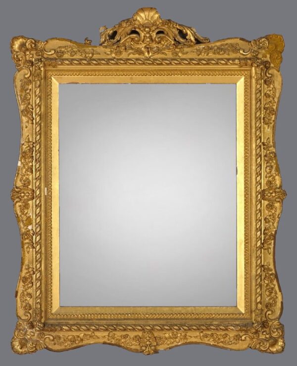 A gold framed mirror with ornate design on the top.