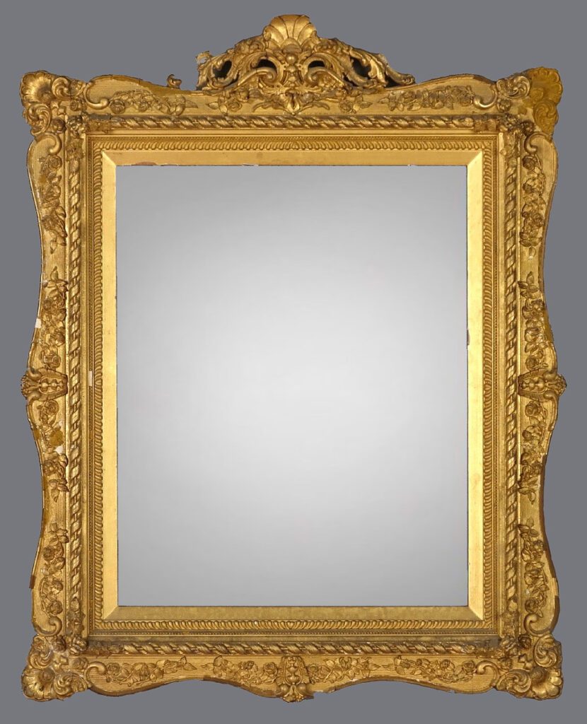 A gold framed mirror with ornate design on the top.