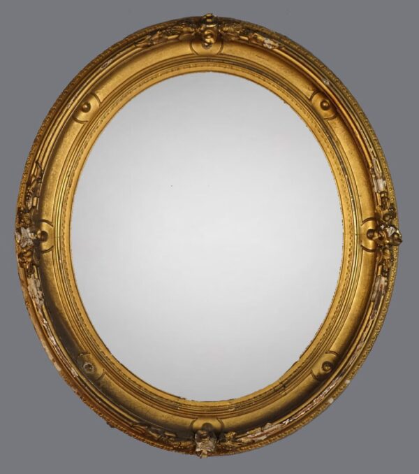 A gold oval mirror with ornate frame and gray background