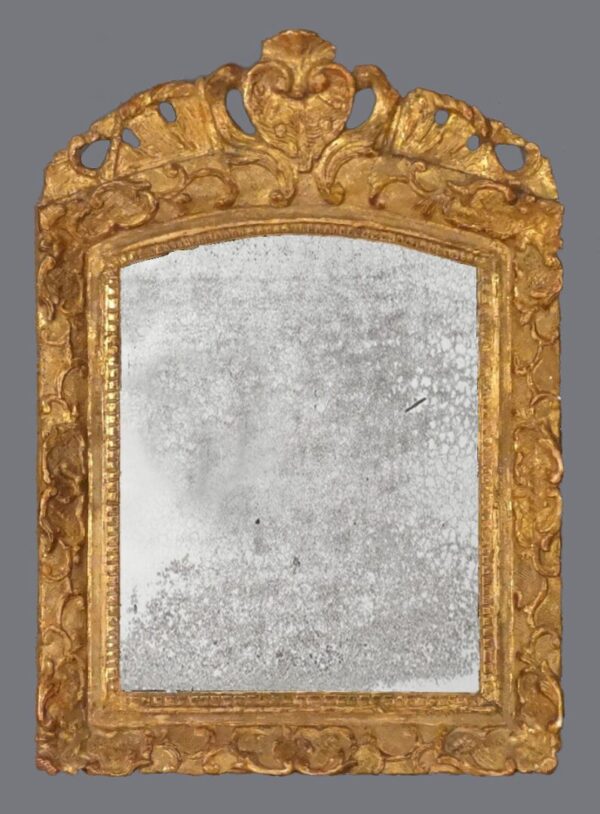 A mirror with gold leaf and an ornate frame.