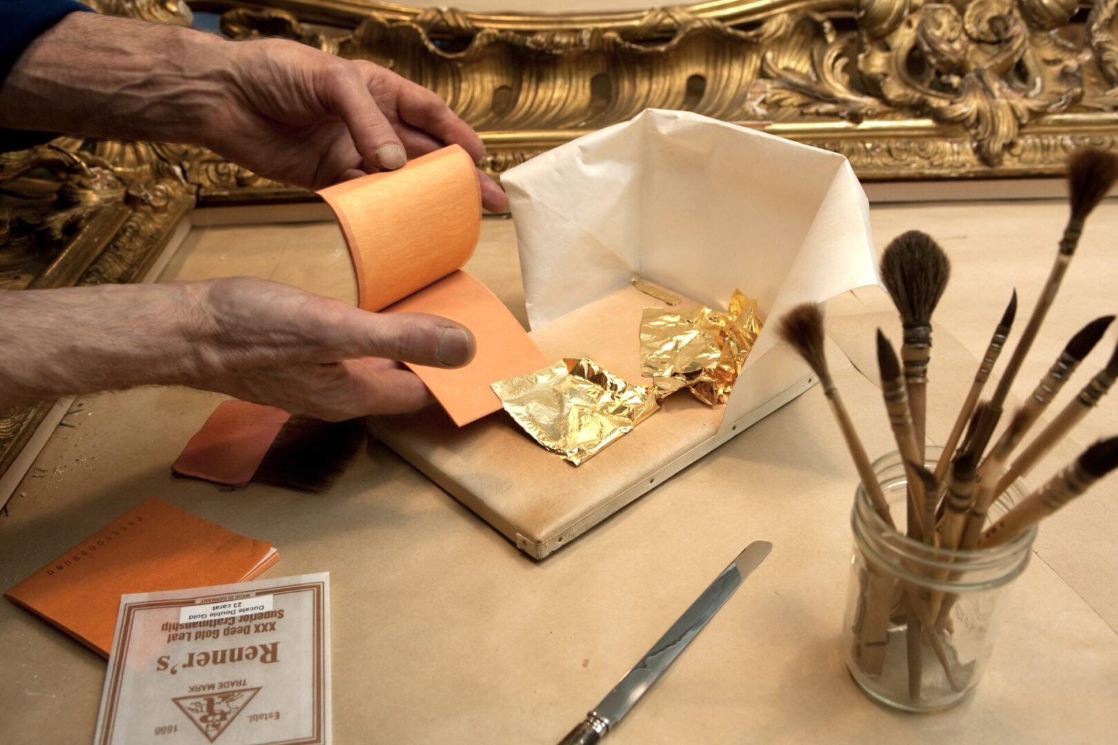 A person is wrapping gold leaf onto paper.